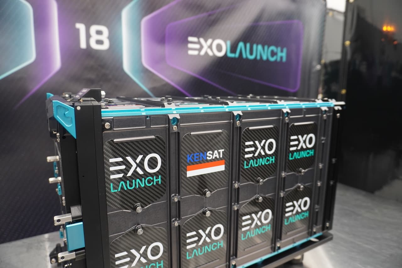 Close-up of the EXOLaunch dispenser with the KENSAT door panel, in front of a Transporter-18 banner