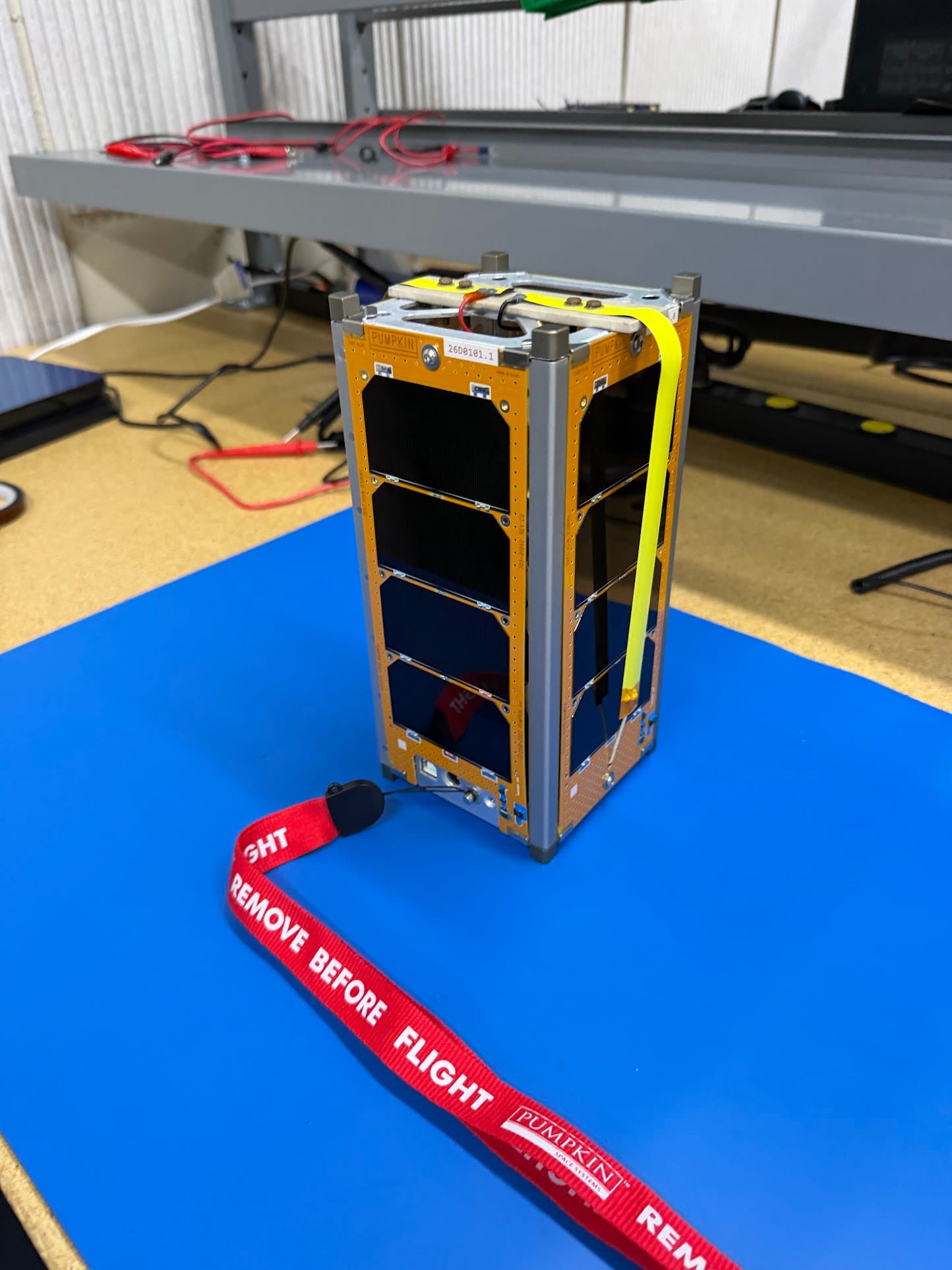 The 2U CubeSat flight unit standing on a blue ESD mat with a remove-before-flight tag